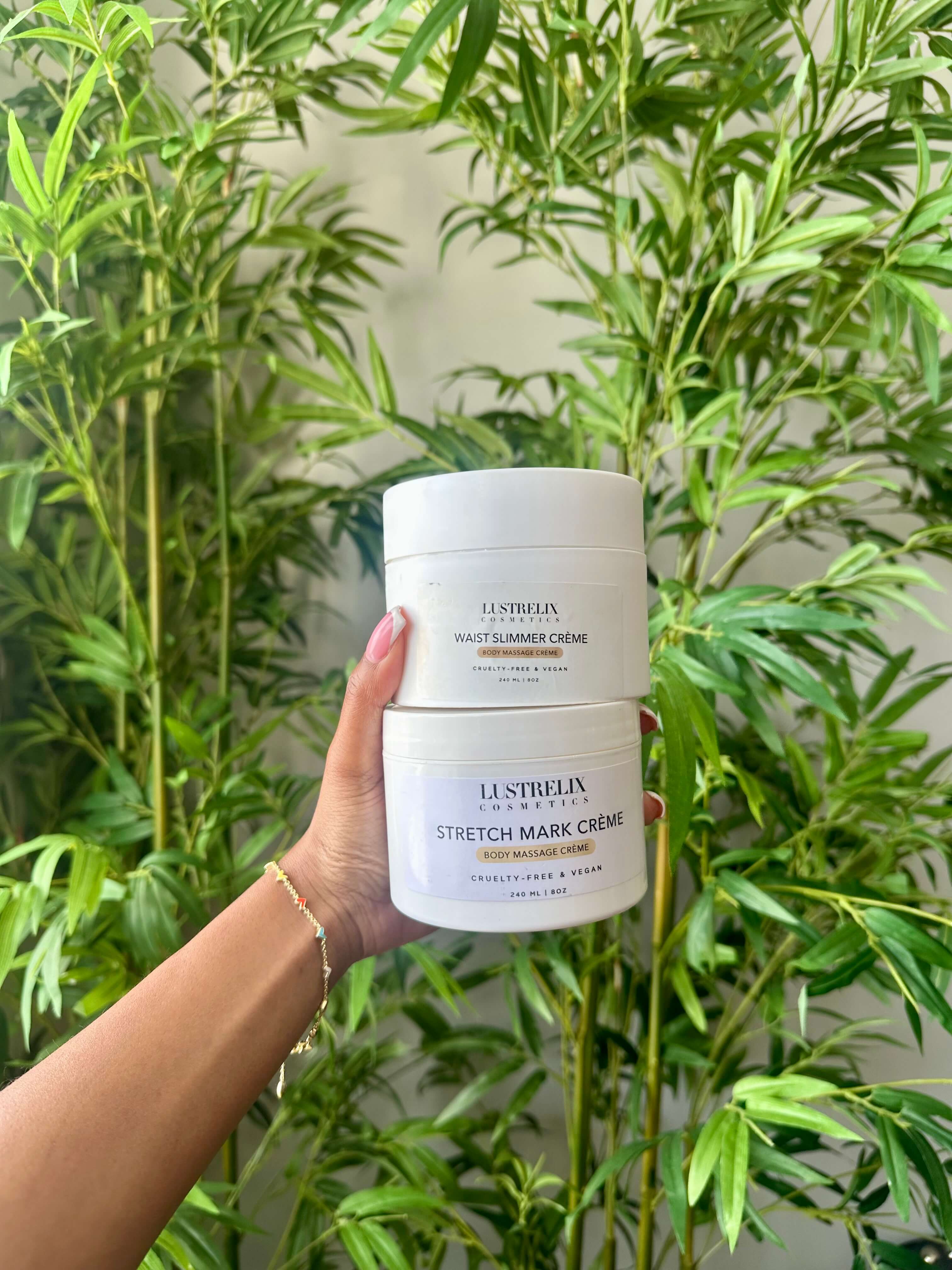 Hand holding a container Lustrelix Cosmetics Stretch Mark Creme against a green leafy background.